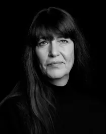 En närbild på en kvinna med långt mörkt hår och lugg, klädd i polotröja.