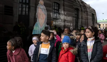 En samling barn i olika åldrar väntar framför en buss på trottoaren.