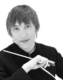 A close-up of a short-haired woman holding a conductor's baton in her hand.