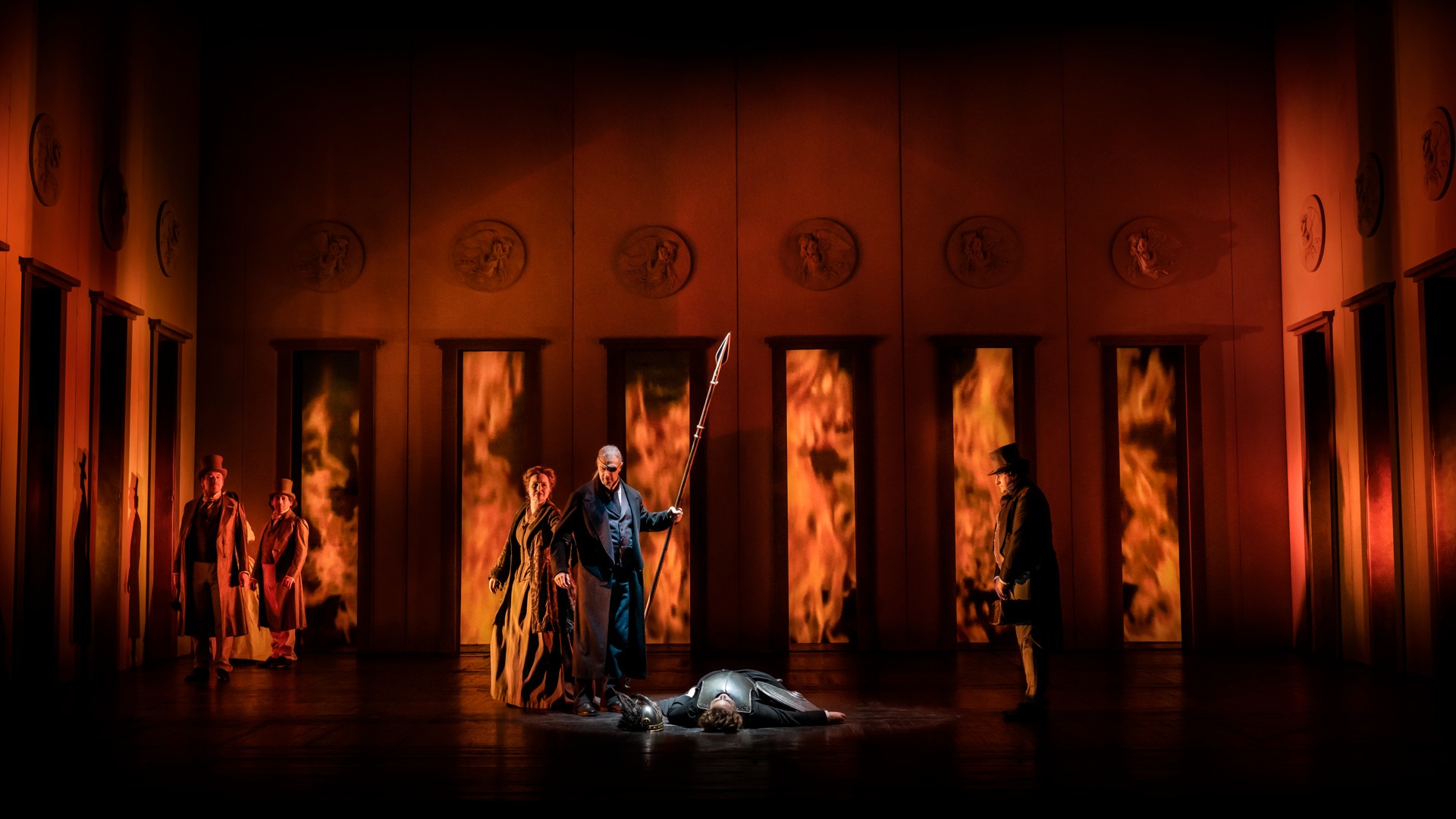 En grupp människor som står på en scen, eld i bakgrunden.