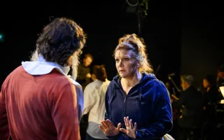 A man in red stands with his back turned to us, a woman in a blue hoodie appears to be talking to him.