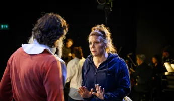 En man i rött står med ryggen vänd mot oss, en kvinna i blå hoodie verkar prata med honom.