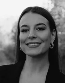 Närbild på en kvinna med långt mörkt hår och örhängen, klädd i mörk kavaj.