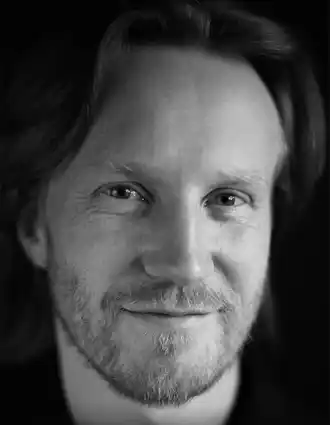 Extrem närbild på en leende man med skägg som bär en mörk skjorta.