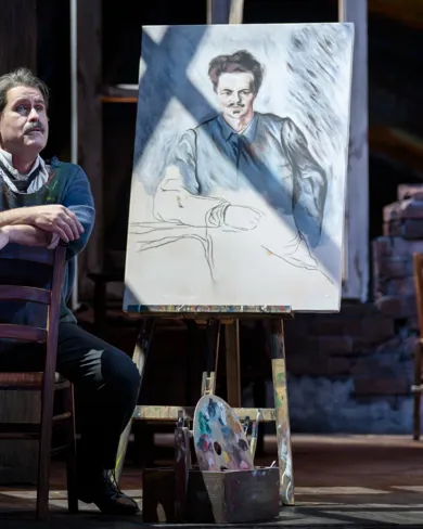 A man sits in front of a painting on an easel.