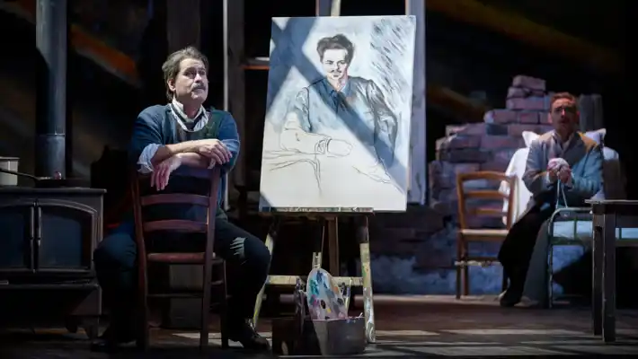 En man sitter framför en målning på ett staffli.