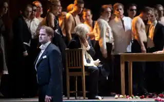 A sad man in a suit stands in front of a large crowd.