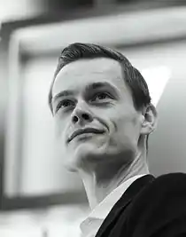 En närbild på en man, tagen lätt underifrån: han bär kostym och blickar uppåt, utåt.