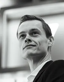 A close-up of a man, taken slightly from below: he is wearing a suit and looking upwards, outwards.