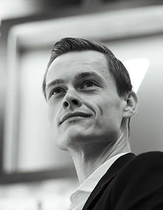 A close-up of a man, taken slightly from below: he is wearing a suit and looking upwards, outwards.