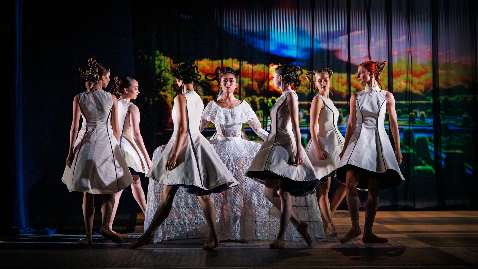 En kvinna i en stor vit klänning är omringad av flickor klädda i korta vita klänningar.