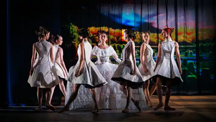 En kvinna i en stor vit klänning är omringad av flickor klädda i korta vita klänningar.