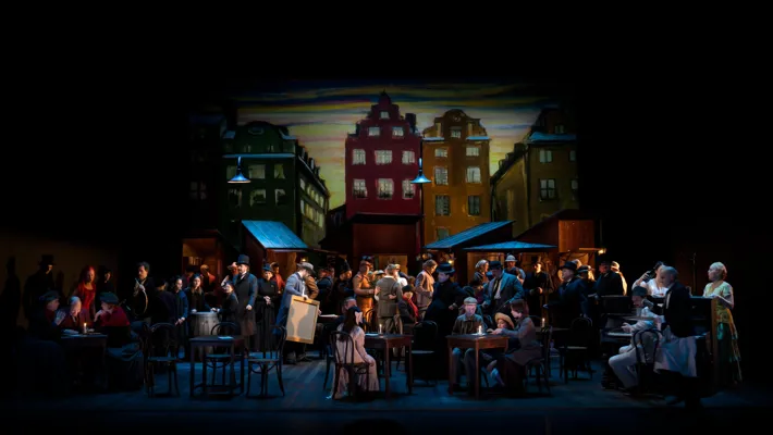 A group of people on a stage - in the background house facades.