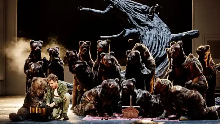 Framför ett knotigt träd står flera björnar, några har picknick, en annan spelar på en liten celesta.