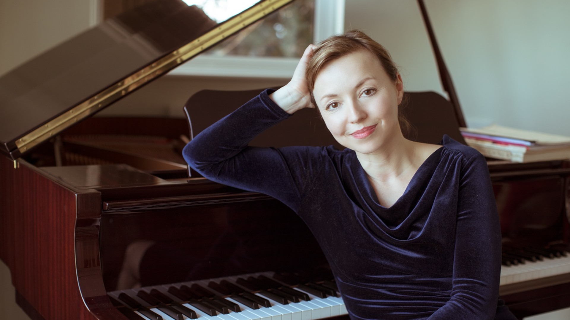 A woman sits leaning against a piano.