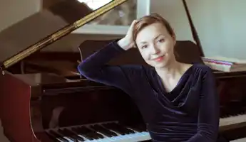 En kvinna sitter lutad mot ett piano.