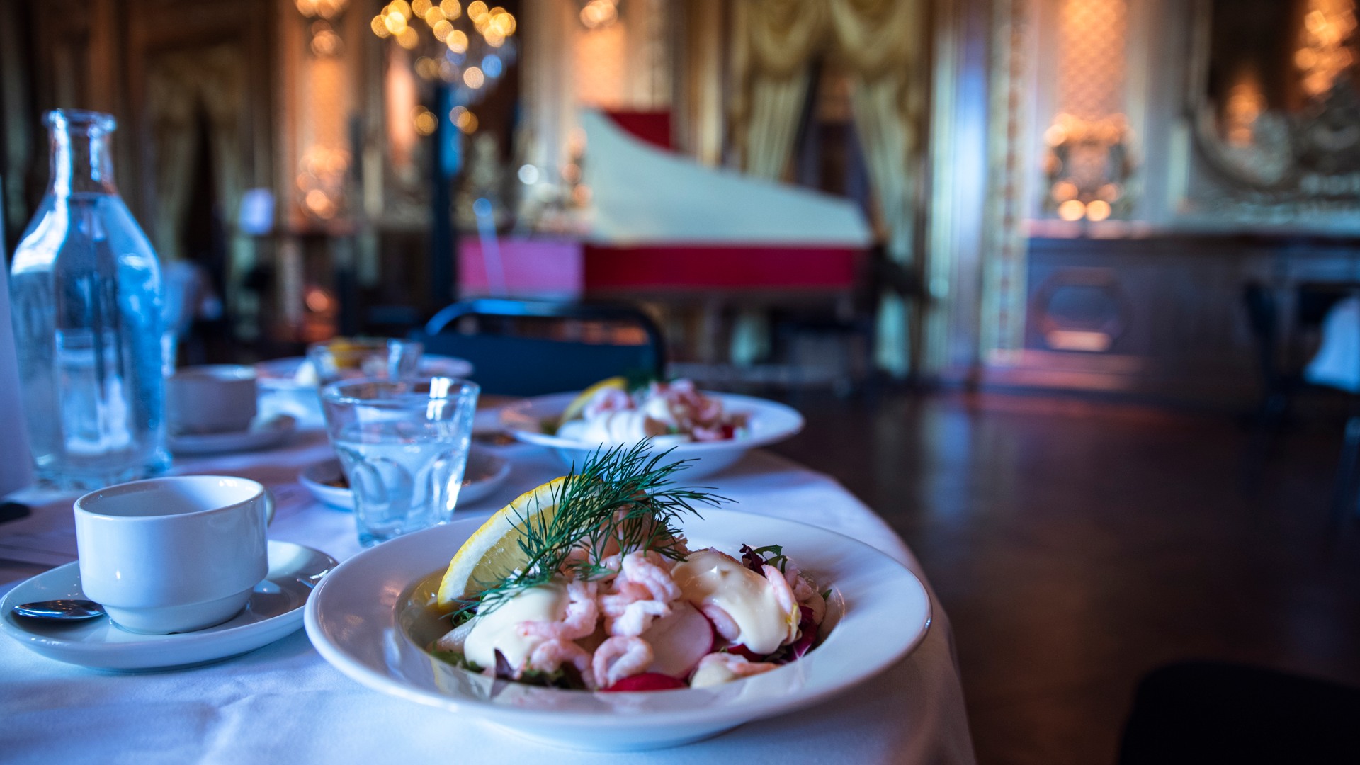 A table set with a shrimp salad, a glass of water and a coffee cup.