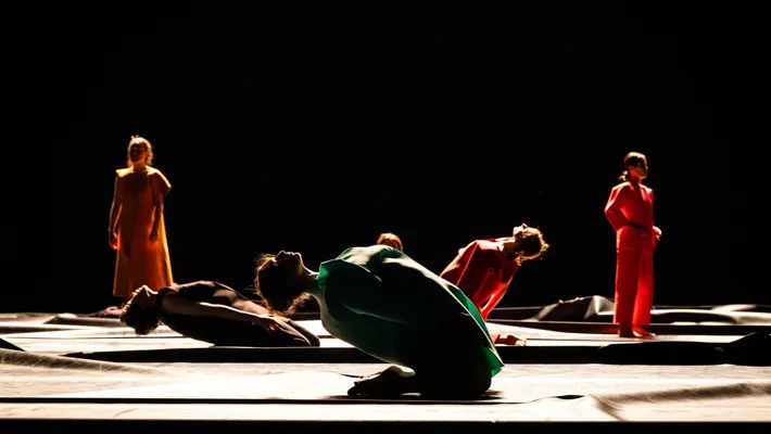 Several dancers move on a stage, some lying down, some standing up.