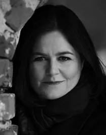 En närbild på en kvinna i mörka kläder, hos står delvis bakom en mur på vänster sida.