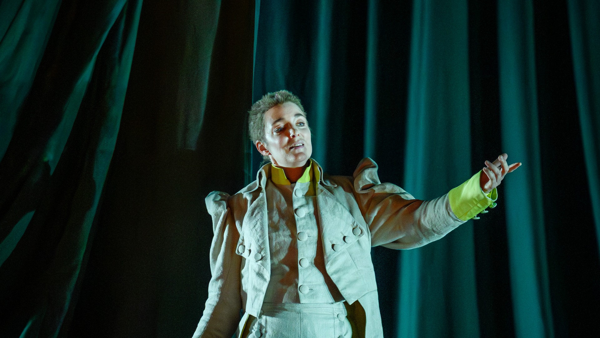 En ung man i kostym står mot ett mörkgrönt tygstycke och sträcker ut vänsterhanden.