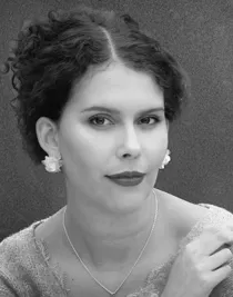 En närbild på en mörkhårig kvinna med uppsatt hår som bär ett halsband och örhängen.