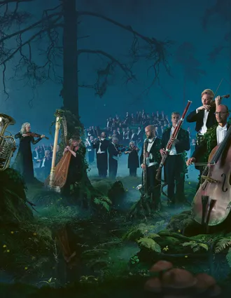 En stor mängd musiker som står och sitter i ett skogslandskap.