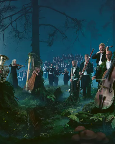 En stor mängd musiker som står och sitter i ett skogslandskap.