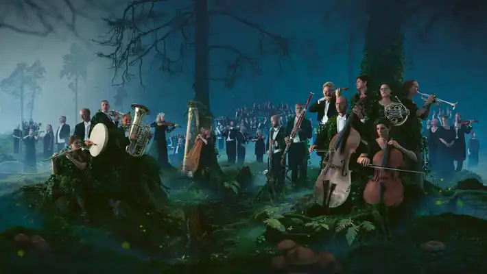 En stor mängd musiker som står och sitter i ett skogslandskap.