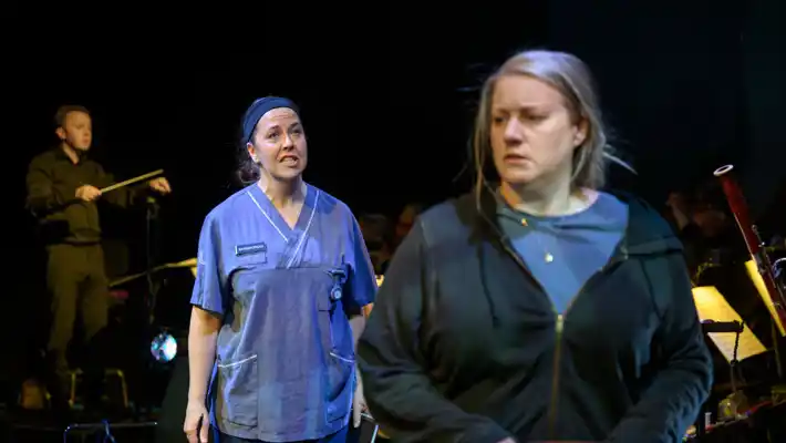 En kvinna i sjukhuskläder står snett bakom en annan kvinna, i vanliga kläder.