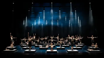 A large number of dancers are placed on cubes on the stage floor - above them spotlights.