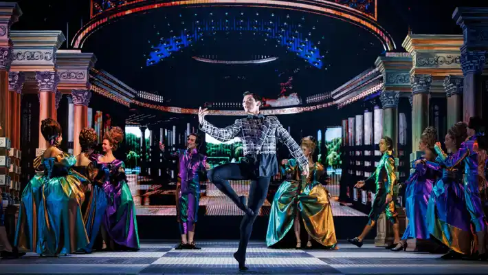 I en rikt utsmyckad sal dansar en man i mitten, omgiven av uppklädda personer.