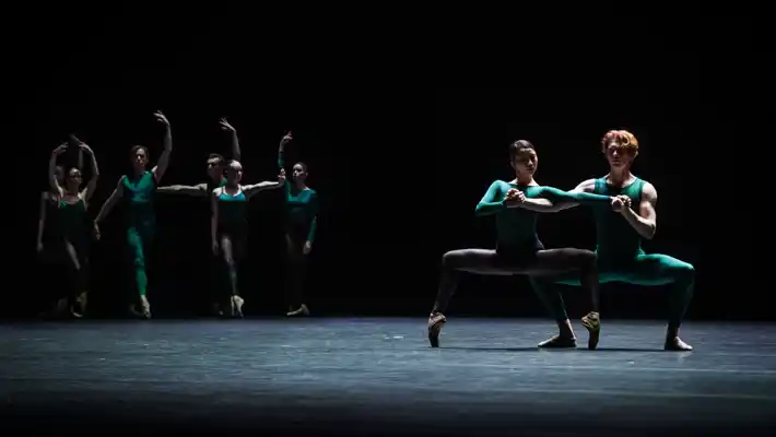 En mörk scen med två dansare i förgrunden och fyra i bakgrunden.