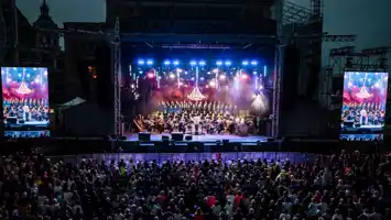En stor mängd människor framför en upplyst scen, på sidorna två stora videoskärmar.