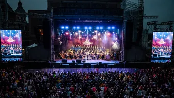 En stor mängd människor framför en upplyst scen, på sidorna två stora videoskärmar.