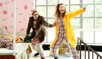 Two people in motion, the one on the right is wearing a yellow raincoat and pointing upwards.