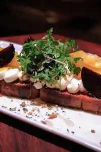 A sandwich with cheese, vegetables and topped with greens on a white plate.