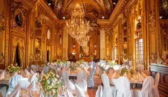Large room with chandeliers and many laid tables with beautiful flower decorations.