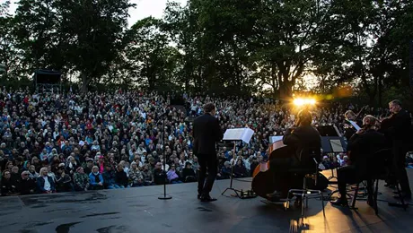 Flera musiker på en utomhusscen ser ut över ett publikhav.