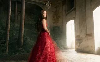 En kvinna i röd klänning står i ett rum med fönster, i vänstra hörnet växer en skog.