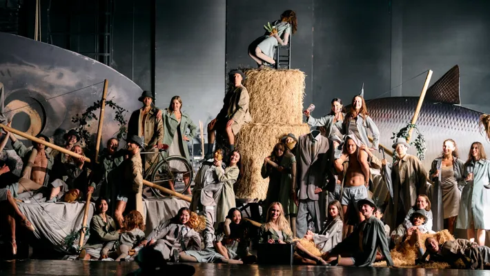 A lot of people on a stage, in the middle large hay bales, in the background a large fish.