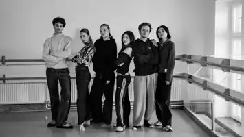 A black and white image of six young men and women standing lined up against a white wall.