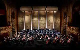 En stor orkester spelar på en scen som är omgärdad av gulddekorationer - i fonden en guldig kuliss.