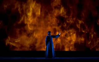 A woman standing in front of a fire filled wall, ring in the right hand.