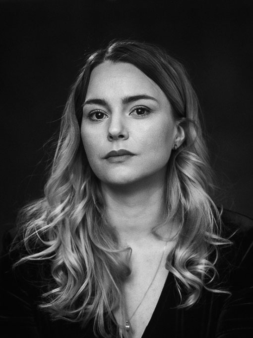 Close-up of a woman with long hair wearing a dark sweater and a necklace.
