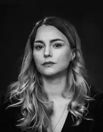 Närbild på en kvinna med långt hår klädd i mörk tröja och bär ett halssmycke.