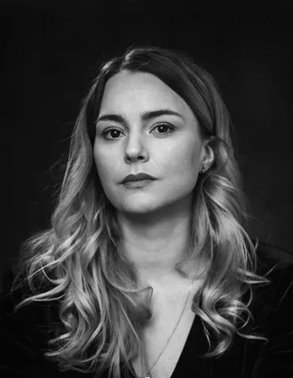 Närbild på en kvinna med långt hår klädd i mörk tröja och bär ett halssmycke.