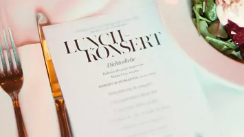 En tallrik med mat står på ett bord tillsammans med kniv, gaffel och ett konsertprogram.