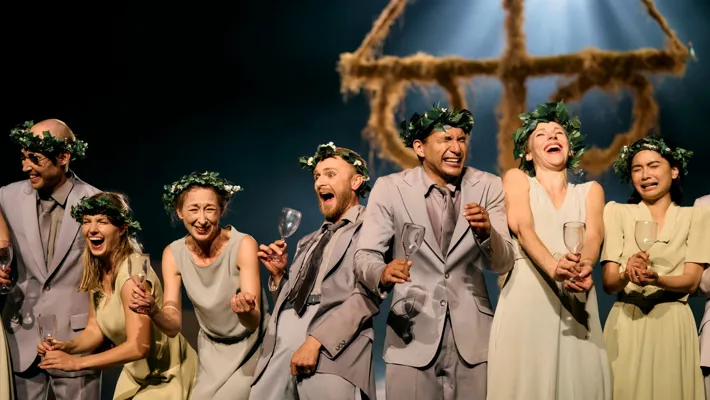 Several people are standing with wine glasses in their hands, laughing and grimacing, in the background a midsummer pole.