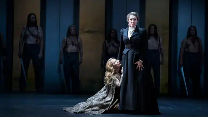 A woman is half-lying on the floor, reaching up towards another woman, pleading.