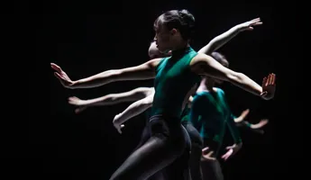 Dansare med gröna kläder mot en mörk bakgrund, de gör rörelser med sina armar.